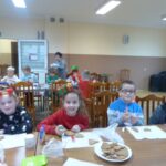 Dzieci siedzą przy stolikach ozdabiając pierniczki.