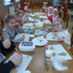 Dzieci siedzą przy stolikach ozdabiając pierniczki.