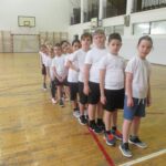 Uczniowie stoją w rzędzie w sali gimnastycznej.